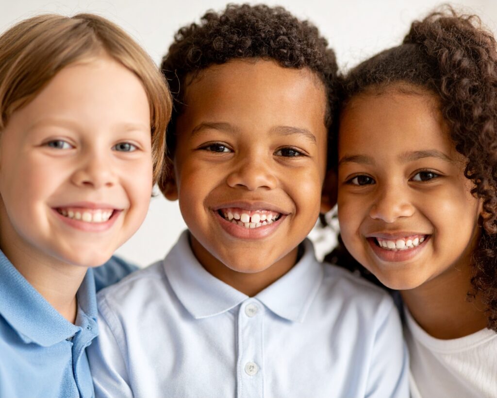 Trois enfants souriants côte à côte. Cette image illustre que chaque patient est unique et que deux sourires qui se ressemblent peuvent nécessiter des traitements orthodontiques différents selon l’occlusion, la croissance des mâchoires et les besoins de chacun.