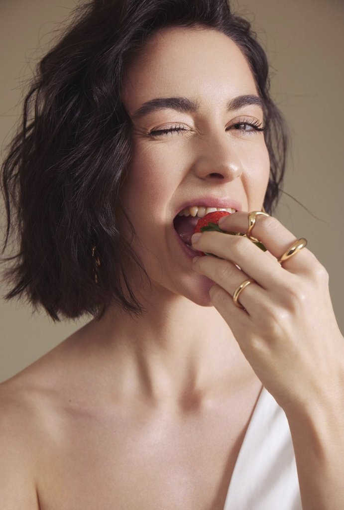 Femme souriante croquant dans une fraise, mettant en évidence les dents et l’occlusion.
